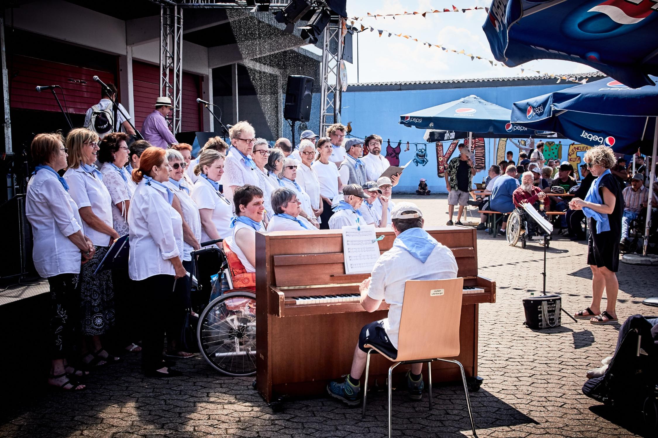 Chor mit verschiedenen Sängerinnen und Sängern steht neben einem Klavier.