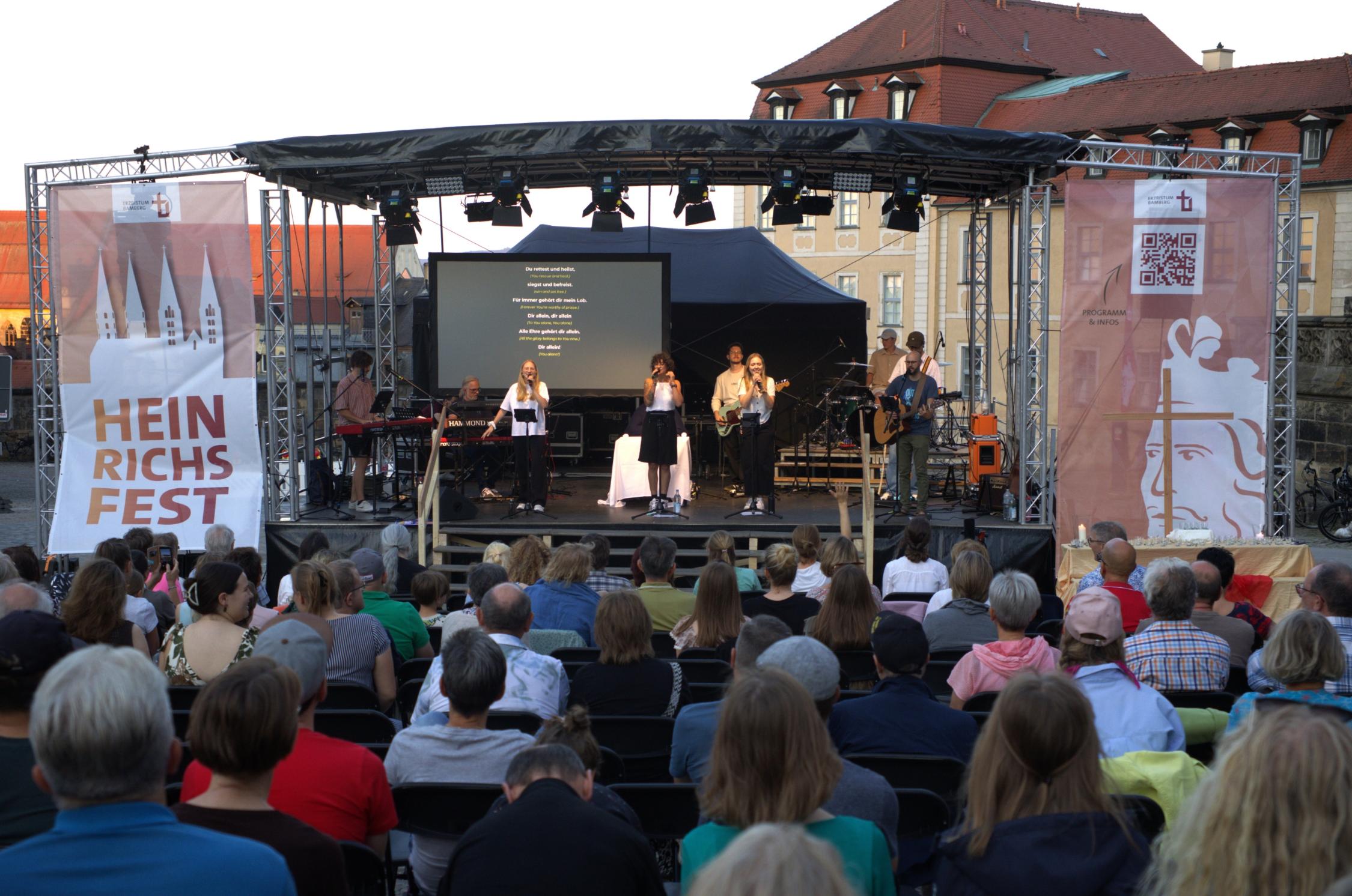 Bühne mit Musikerinnen und Musikern auf dem Domplatz, davor viele Menschen auf Stühlen